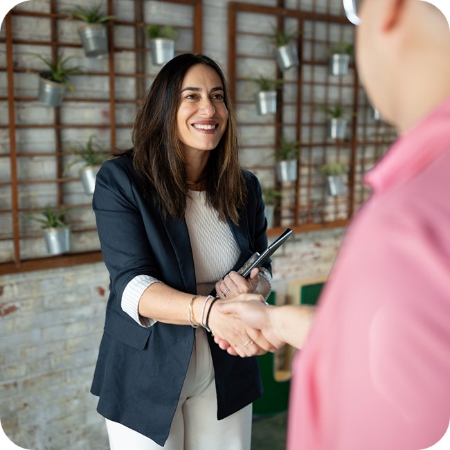 racehl feinman shaking hands with a male business partner in front of a white brick wall decorated with tin planters