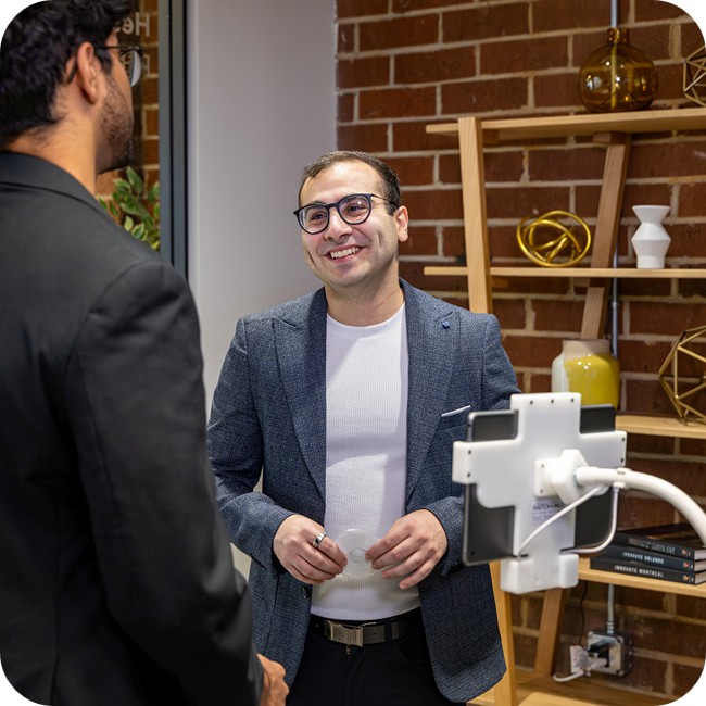 male tgh ventures team members smiling and conversing in front of a brick wall with ornate decorations on a wooden stand with a mounted tablet device in the foreground