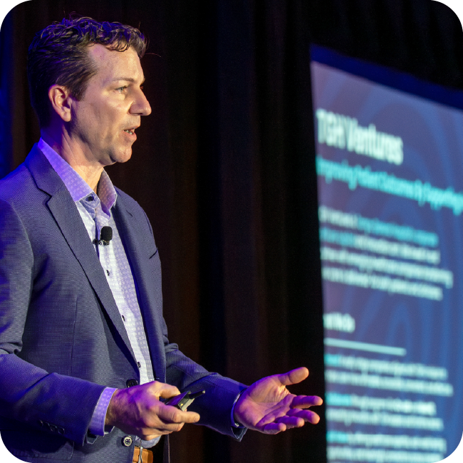 jason swoboda speaking at an event with a screen showing tgh vetures information in the background