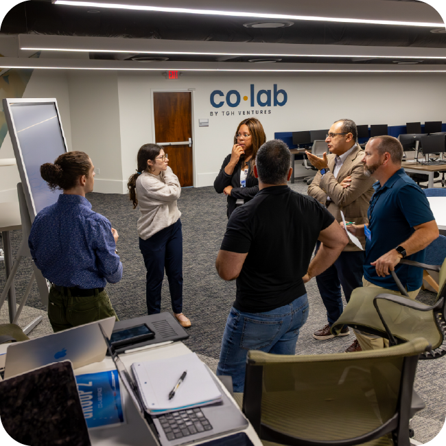 a group of male and female healthcare technology professionals in business casual attire share ideas around a white board in a large conference room