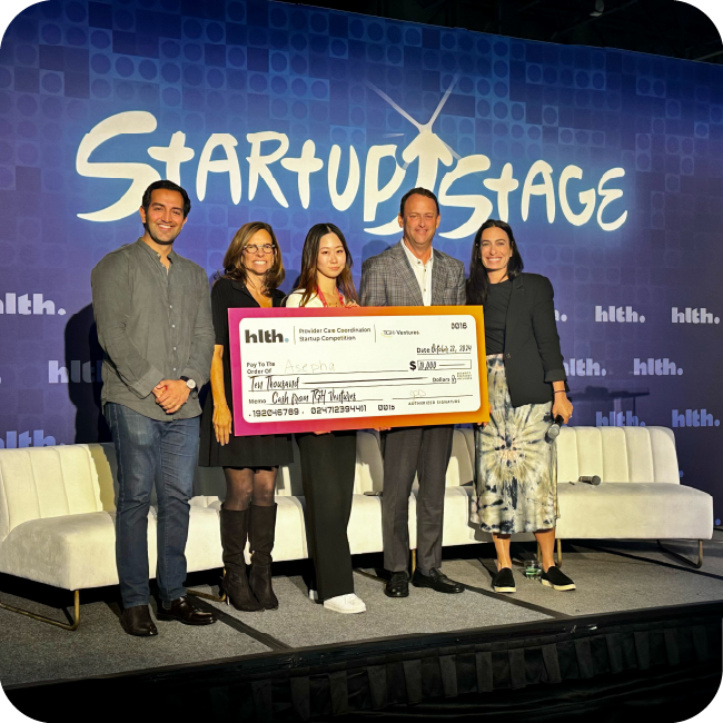 john couris and rachel feinman presenting an oversized check to members of the asepha organization in front of a startup stage background